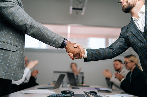 Closeup of unrecognizable African and Caucasian business partners meeting and handshake, applause and partnership success for financial deal or achievement. Trust, support and collaboration.