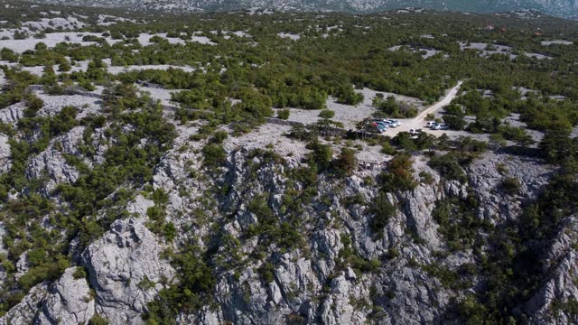A captivating drone view of viewpoint near Paklenica, Croatia's Velebit mountains, featuring cliffs, cars, and lush Mediterranean flora under the summer sun