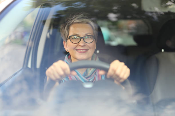 成熟した幸せな女性ドライバーは、美しさと陽気さを放ちながら、豪華な車で旅を楽しんでいます。 - owner women car rear view mirror ストックフォトと画像