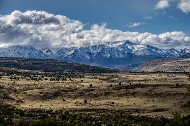 A mountain range in warm tones with a background of cold blue Andes mountains covered in snow.