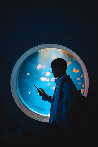 A man is holding a mobile phone at the aquarium to search for information on marine life - weekend activities, travel life, people and life