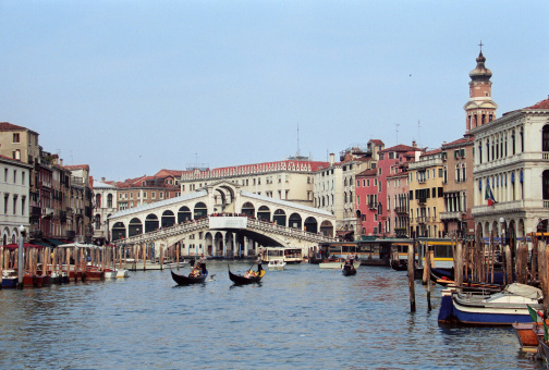 The Venetian Gondoliere with tourists in gondola at the Canale Grande of Venice, Italy. In the background is the world famous Rialto Bridge. Gondolas are the classical Venetian boats and are now mostly used for tourists.