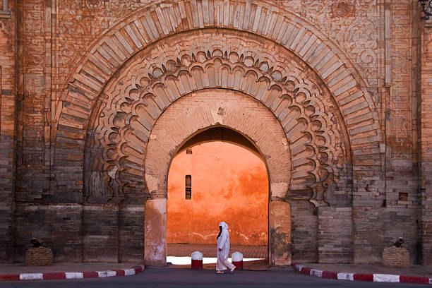 Bab Agnaou Woman in traditional arab clothing with veil passing by the Bab Anaou gate in Marrakech. The woman walks right in the middle of the gate that is colored orange by the late sunlight. casbah photos stock pictures, royalty-free photos & images