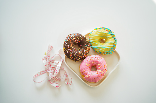 colorful donuts and tape measure. unhealthy foods weight gain
