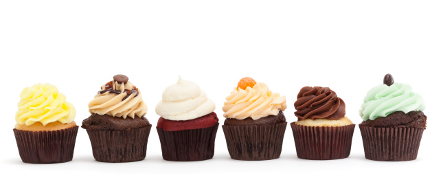 Photograph of 6 pretty, gourmet cupcakes in a row on a white background; copy space 