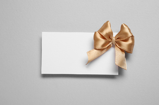 Blank gift card with golden bow on light grey background, top view. Space for text