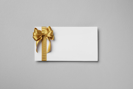 Blank gift card with golden bow on light gray background, top view