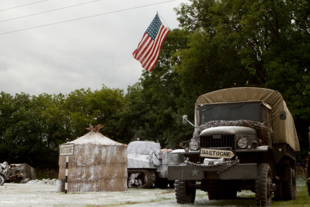A world war 2 era truck in the snow by a sign to Bastogne. Battle of the Bulge scenario. Re-enactment.