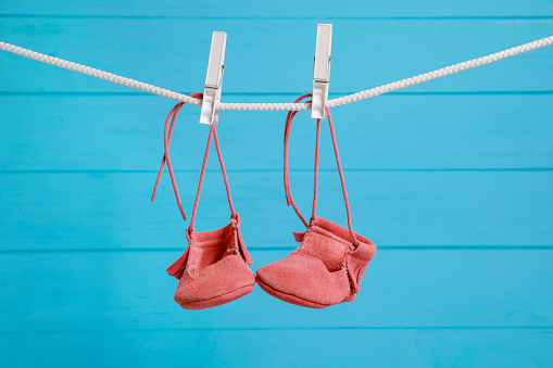 Cute baby shoes drying on washing line against light blue wooden wall