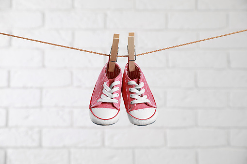 Cute pink baby sneakers drying on washing line against white brick wall