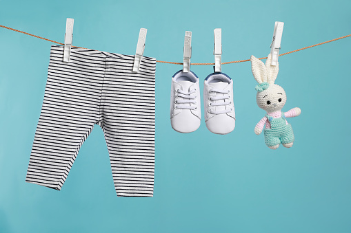 Striped baby pants, shoes and crochet toy drying on washing line against turquoise background