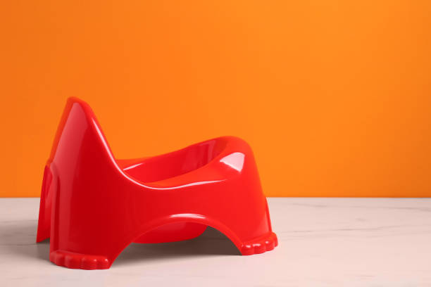 istock Red baby potty on white marble table against orange background, space for text. Toilet training 1683171847