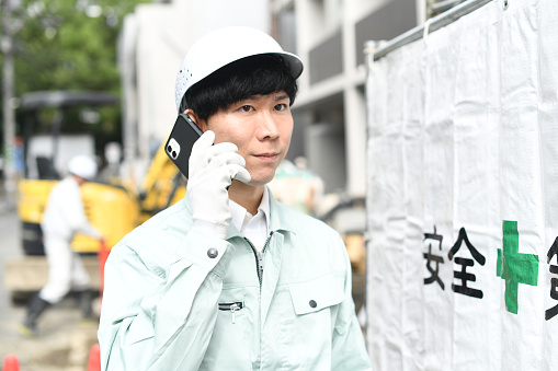 Young Asian male worker making a phone call at a construction site