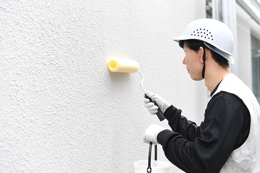 Asian male worker painting exterior walls outdoors