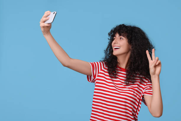 istock Beautiful young woman taking selfie on light blue background 1683219242