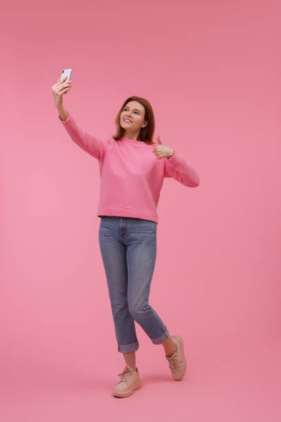 istock Beautiful woman taking selfie on pink background 1683225561