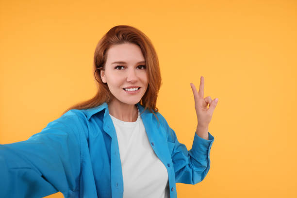 istock Beautiful woman taking selfie on orange background 1683228218