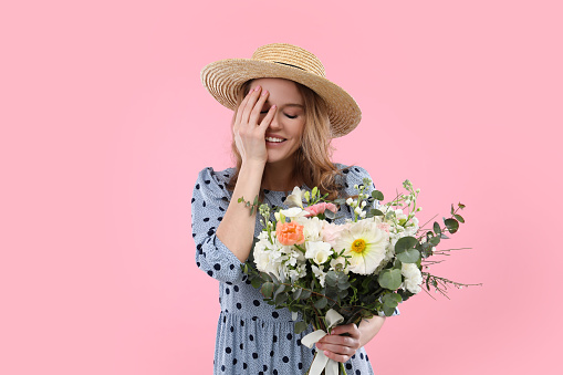 Beautiful woman in straw hat with bouquet of flowers on pink background