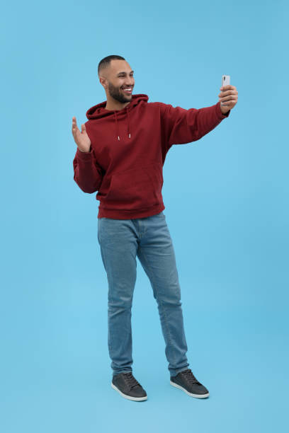 istock Smiling young man taking selfie with smartphone on light blue background 1683237274
