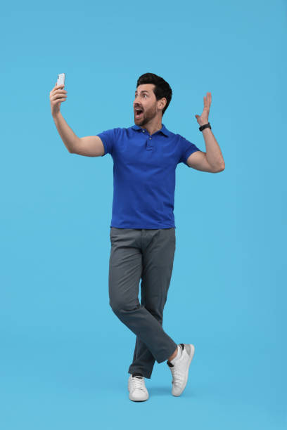 istock Surprised man taking selfie with smartphone on light blue background 1683247047