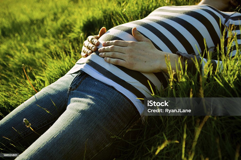 Pregnant Belly at Sunset A young woman, halfway through her pregnancy, lays in a field of green grass holding her hands on her stomach, the summer sun shining warmly on her.  Horizontal with copy space. Abdomen Stock Photo