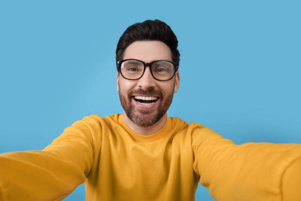 istock Smiling man taking selfie on light blue background 1683248109