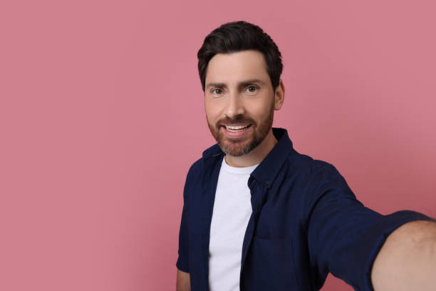 istock Smiling man taking selfie on pink background, space for text 1683248619