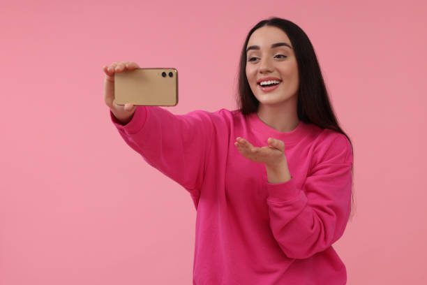istock Smiling young woman taking selfie with smartphone on pink background, space for text 1683271439