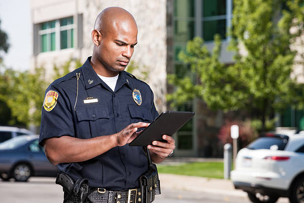Police Officer Using Computer Tablet A mid-adult male african american law enforcement officer uses a modern electronic touch screen tablet to enter a citiation or look up information while outdoors. electronic organizer photos stock pictures, royalty-free photos & images