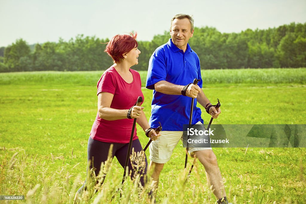Active seniors doing nordic walking Mature couple enjoying nordic walking in a countyside. Looking at each other and smiling. Nordic Walking Stock Photo