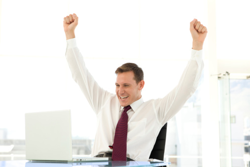 Ecstatic young businessman raising arms at workplace