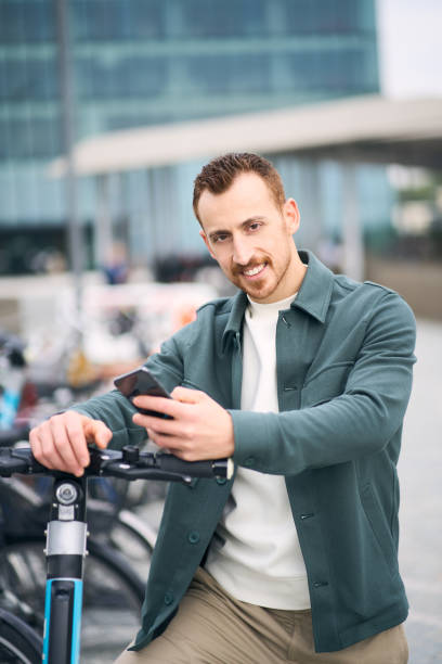 istock Smiling modern man holding mobile phone standing near electric scooter 1683308691