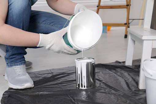 Man pouring white paint from bucket into can indoors, closeup