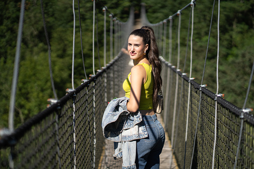 an adventurous young woman watching as she walks across a suspension bridge