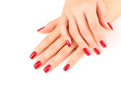 Set of nicely manicured fingernails of adult caucasian woman painted in red over white background. One hand is placed over other. Top view.