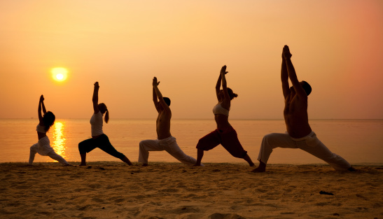 Five people practising yoga at the beach - warrior I pose.
