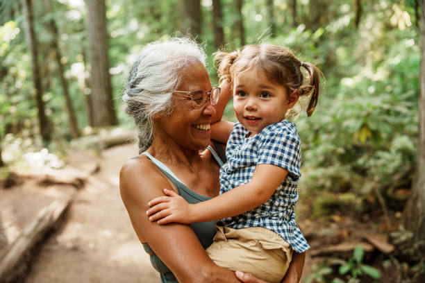 Vibrant Pacific Islander senior woman hiking with Eurasian granddaughter A healthy and adventurous senior woman of Hawaiian and Chinese descent laughs joyfully while carrying her adorable three year old Eurasian granddaughter during a hike through a lush forest in Oregon. young grandparents stock pictures, royalty-free photos & images
