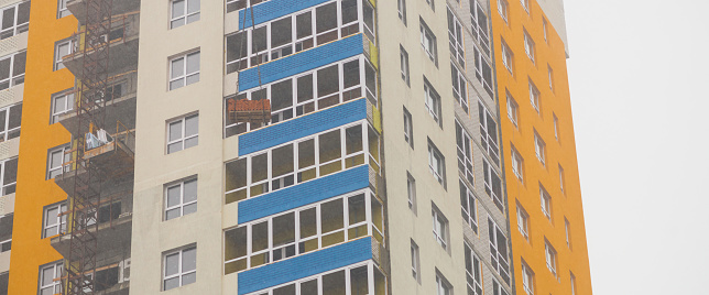 Concept of apartment building under construction close-up. Exterior of multicolor new multi-story residential building. Background with yellow walls, white plastic windows and blue loggias. Copy space