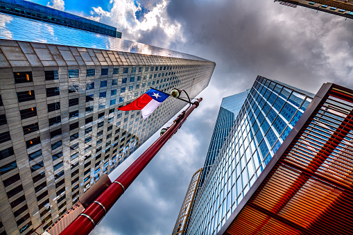 View of two large skyscrapers from shot from below with the Texas flag hung from a street lamp in downtown Houston, Texas