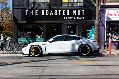 A white Porsche Taycan, Porsche's first electric vehicle model, is seen parked in downtown Toronto on a sunny day.