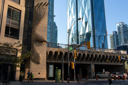 The morning sun shines off a newly constructed office building in downtown Toronto, as a bird in stone is seen on the side of the building, street level.