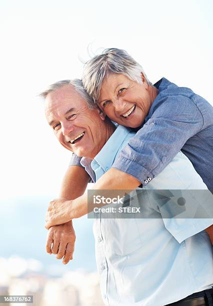 Smiling Senior Man Giving Piggeback Ride To Woman Outdoors Stock Photo - Download Image Now