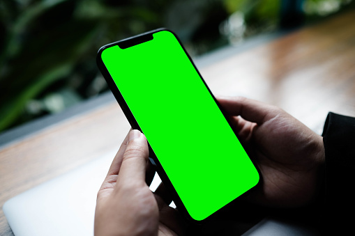 Imagen de maqueta de una gente de negocios sosteniendo un teléfono móvil inteligente con pantalla verde en blanco en una mesa de madera vintage en un moderno restaurante cafetería durante la reunión o el almuerzo. photo