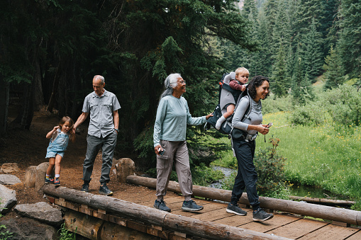 An active and happy multiracial, multigenerational family hike across a small bridge, looking at the beautiful surrounding nature while bonding on a family camping vacation.