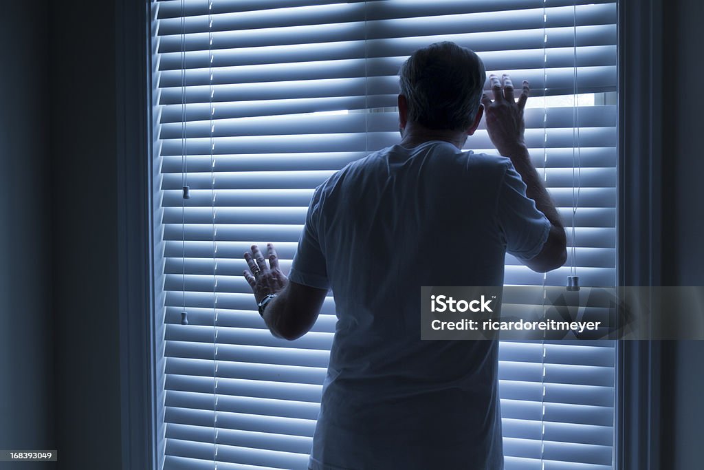 Homeowner Nervously Checks On Outside Noise Late At Night This nervous homeowner checks on unusual sounds outside his home late at night, concerned about possible burglary or break in. 55-59 Years Stock Photo