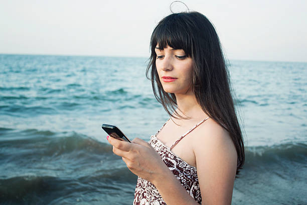 Beautiful young woman writing a text message at the beach