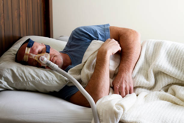 Man Sleeping in Bed with Sleep Apnea Mask Photo of a man sleeping while wearing a CPAP mask. sleep apnea photos stock pictures, royalty-free photos & images