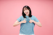 Smiling beautiful young asian woman showing thumbs up isolated on pink background.