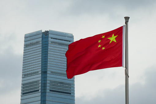 The flag of the People's Republic of China on a flagpole in Admiralty on Hong Kong Island.  In the background is the International Commerce Centre in Kowloon   This image was taken on an overcast afternoon on 14 September 2023.