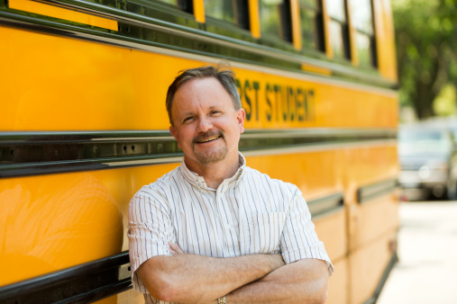 Portrait of a school bus driver standing next to a school bus smiling at camera.